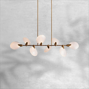 Lyla linear chandelier lit, warm glow through alabaster petal shades on aged brass stem