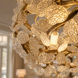 A circular gold metal chandelier with frosted glass leaf accents suspended by thin cables.