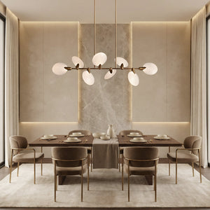 Lyla brass linear chandelier with alabaster petals above a beige dining table with marble accent wall