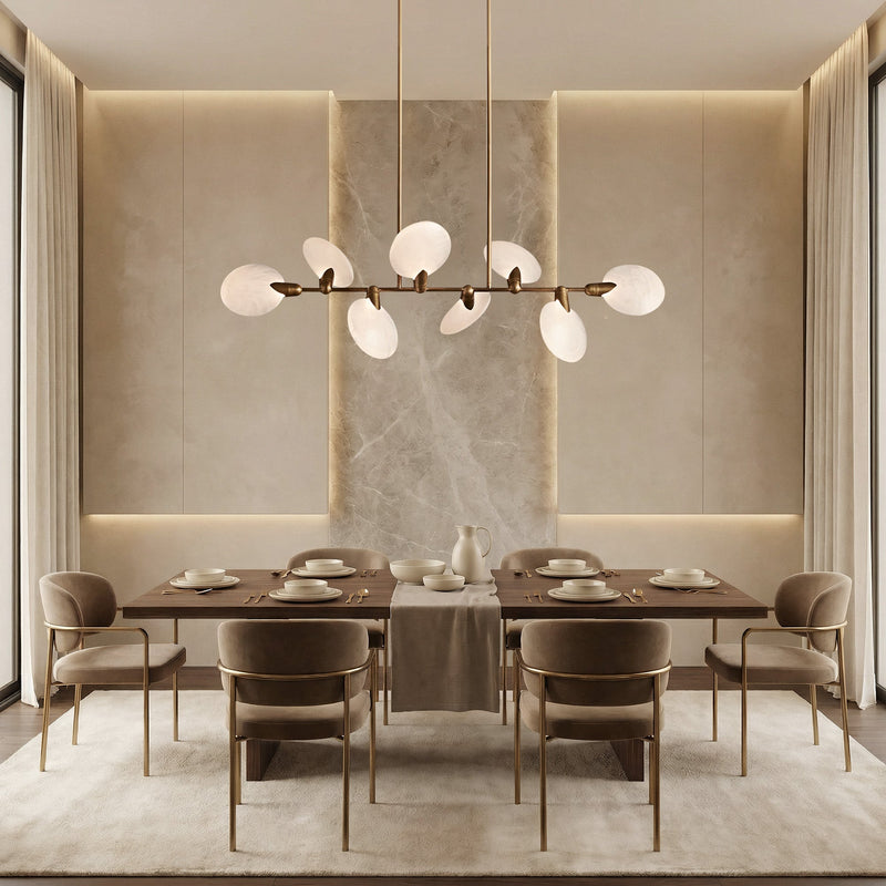 Lyla brass linear chandelier with alabaster petals above a beige dining table with marble accent wall