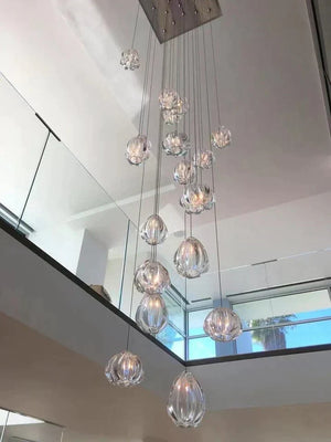 Hand-blown glass teardrop cluster chandelier hanging in a double-height stairwell with mirror wall