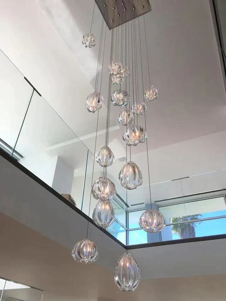 Hand-blown glass teardrop cluster chandelier hanging in a double-height stairwell with mirror wall