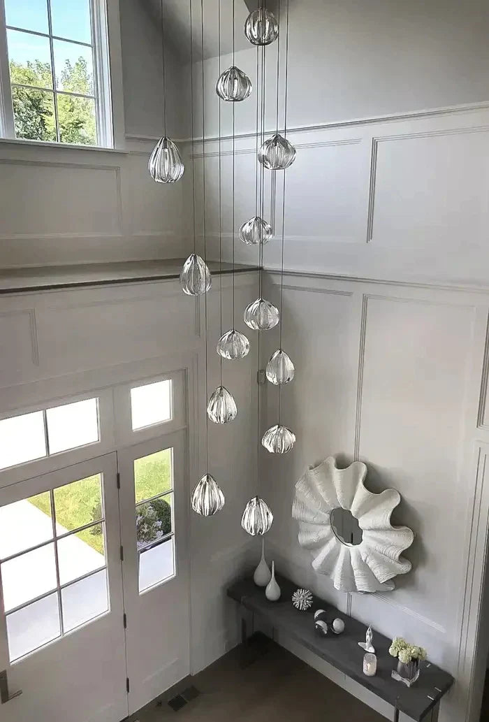 Long glass pendant chandelier in a white entryway with double-height wainscoting