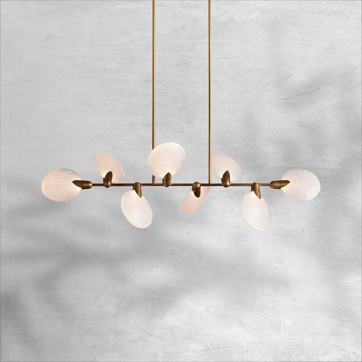Lyla linear chandelier lit, warm glow through alabaster petal shades on aged brass stem