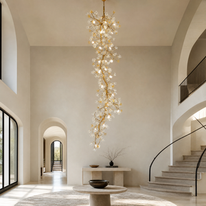 A tall gold cascading chandelier featuring metallic branches and crystal glass blossoms hanging in a high-ceiling space.