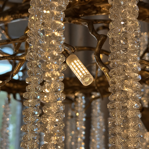A circular antique gold branch chandelier with cascading crystal bead strands hangs from the ceiling in a lit room.