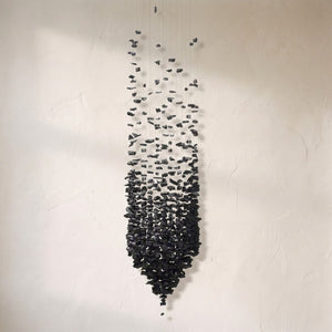 Black stones chandelier, a tapered column of charcoal fragments suspended on fine cables