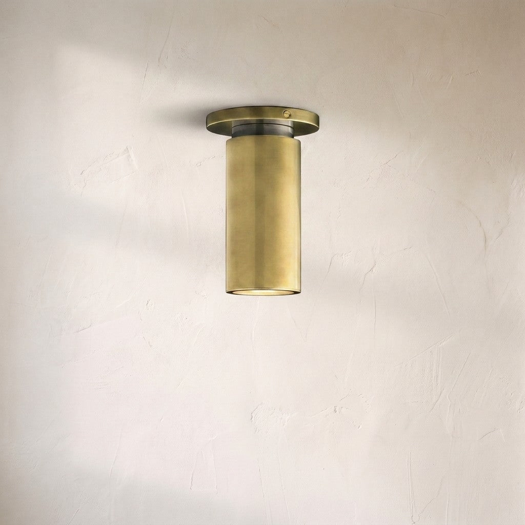 A modern cylindrical wall sconce with a brushed brass finish, mounted on a textured off-white plaster wall.