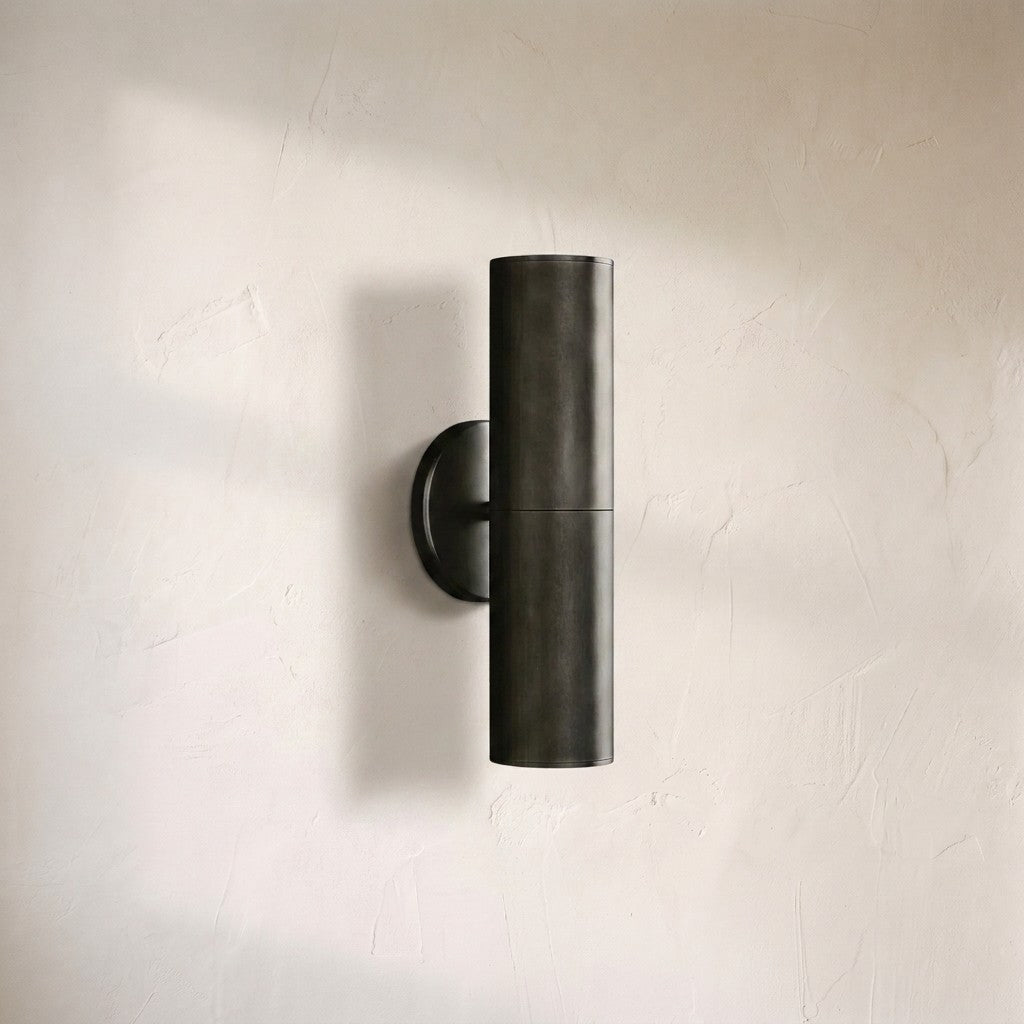 Cenora linear sconce, slim blackened bronze cylinder mounted vertically on a round backplate