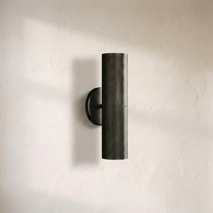 Cenora linear sconce, slim blackened bronze cylinder mounted vertically on a round backplate