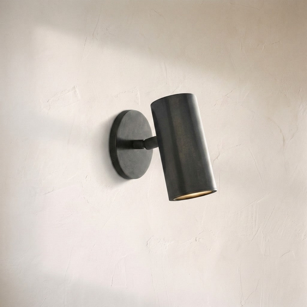 Cenora sconce, single blackened bronze cylinder angled downward on a round wall plate