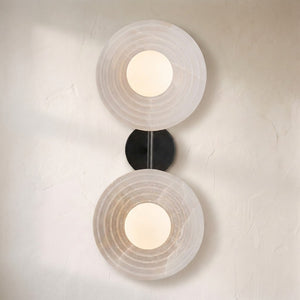 Dahlia double alabaster wall sconce on a plaster wall, two ribbed stone discs with a warm centre glow