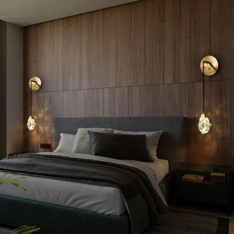 Pair of brass wall sconces with faceted crystal shades on a walnut panelled bedroom wall